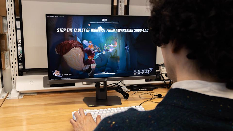 Игровой монитор с текстом 'STOP THE TABLET OF IRON PIST FROM AWAKENING SHOU-LAD' и игроком за клавиатурой