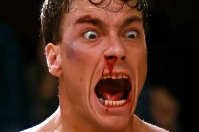 Жан-Клод Ван Дамм с кровью на лице, кричащий в боксерском стиле